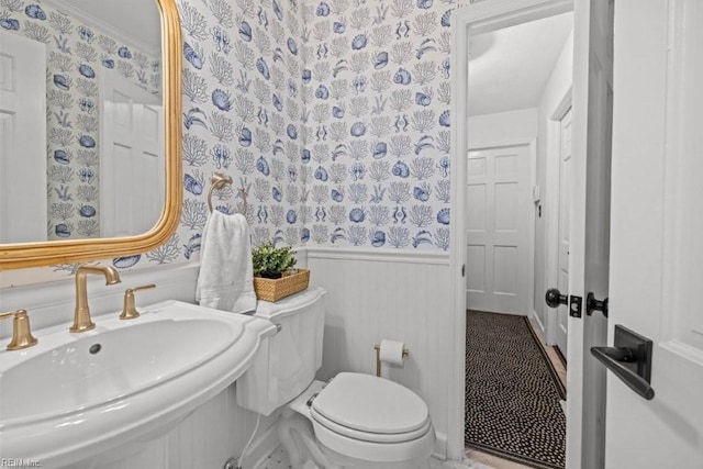 bathroom featuring wallpapered walls, a sink, a wainscoted wall, and toilet