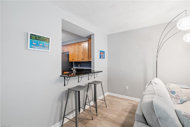 bedroom with light wood finished floors, refrigerator, a textured ceiling, and baseboards