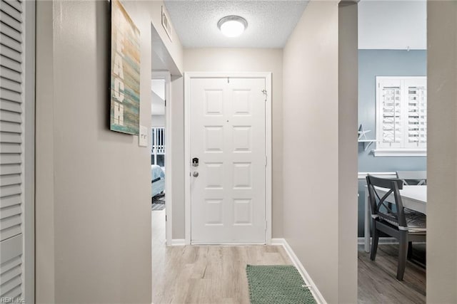 entryway with light wood-type flooring, a textured ceiling, and baseboards