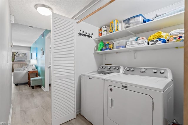 laundry room featuring washer and clothes dryer, light wood-style flooring, a textured ceiling, and baseboards