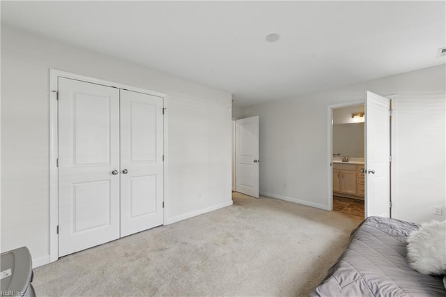 bedroom with light carpet, baseboards, a closet, ensuite bath, and a sink