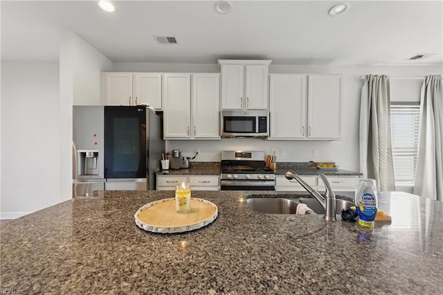 kitchen with appliances with stainless steel finishes, a sink, white cabinets, recessed lighting, and dark stone counters