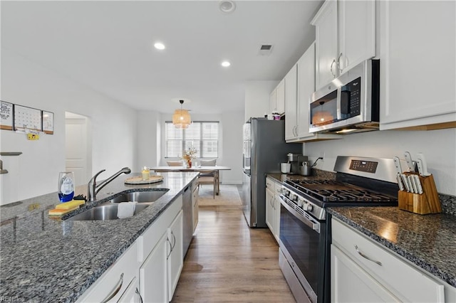 kitchen with appliances with stainless steel finishes, a sink, white cabinetry, recessed lighting, and dark stone countertops