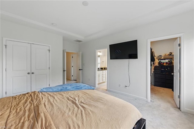 bedroom featuring a closet, light carpet, baseboards, and ensuite bath