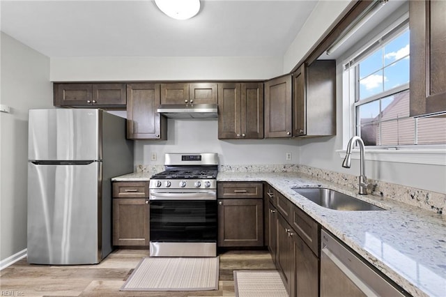 kitchen with appliances with stainless steel finishes, a sink, light wood-style flooring, and dark brown cabinetry