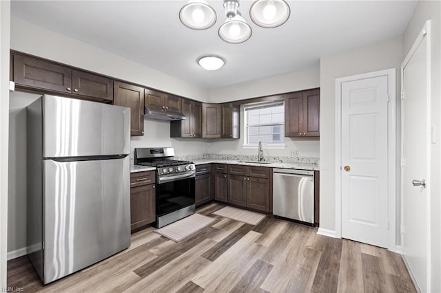 kitchen featuring appliances with stainless steel finishes, under cabinet range hood, dark brown cabinets, light wood-style floors, and a sink
