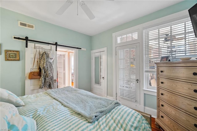 bedroom featuring a barn door, access to outside, baseboards, wood finished floors, and a ceiling fan