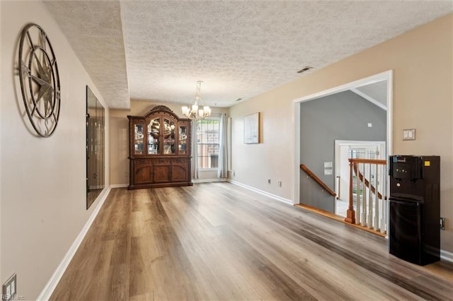 unfurnished dining area with wood finished floors, a chandelier, baseboards, and a textured ceiling