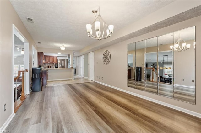 unfurnished living room with a chandelier, light wood finished floors, a textured ceiling, and baseboards