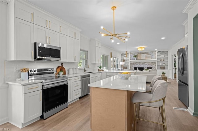 kitchen featuring stainless steel appliances, a chandelier, light wood-style floors, a kitchen island, and crown molding