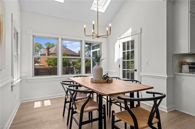 dining space featuring a skylight, light wood-style flooring, a chandelier, baseboards, and lofted ceiling
