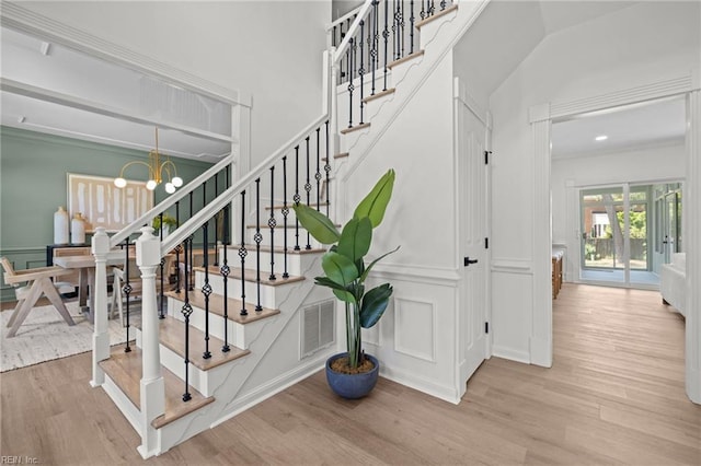 stairs with a decorative wall, wood finished floors, and a chandelier