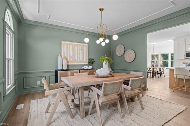 dining room featuring a chandelier, light wood-style floors, ornamental molding, a decorative wall, and wainscoting