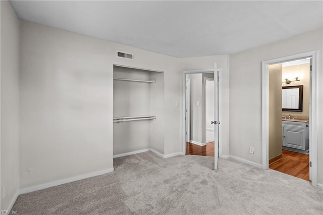 unfurnished bedroom featuring carpet floors, baseboards, a sink, a closet, and ensuite bathroom