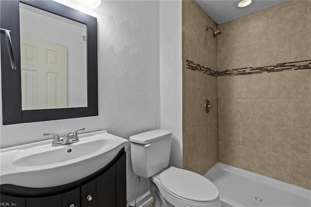 bathroom with toilet, tiled shower, and vanity