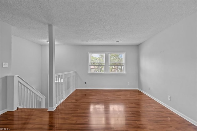 empty room with wood finished floors, a textured ceiling, and baseboards