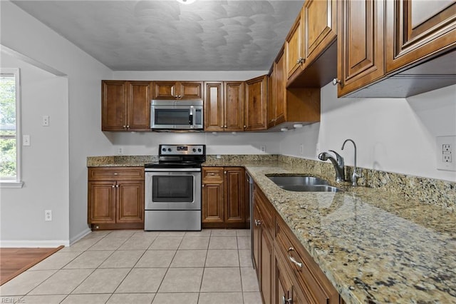 kitchen with stainless steel appliances, a sink, light stone countertops, baseboards, and brown cabinetry