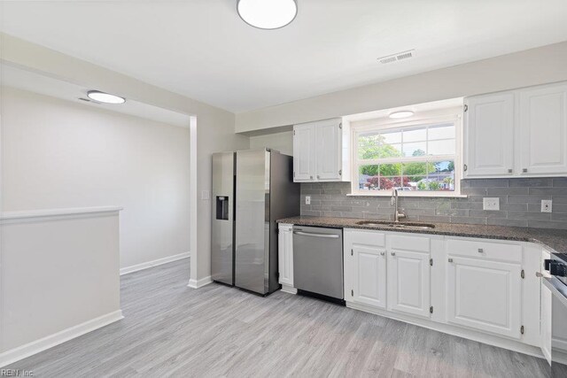 kitchen with a sink, stainless steel appliances, light wood-style flooring, and dark stone countertops