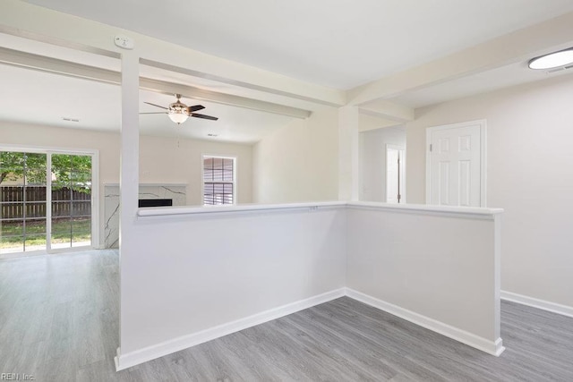 empty room featuring wood finished floors, a ceiling fan, a premium fireplace, baseboards, and beamed ceiling