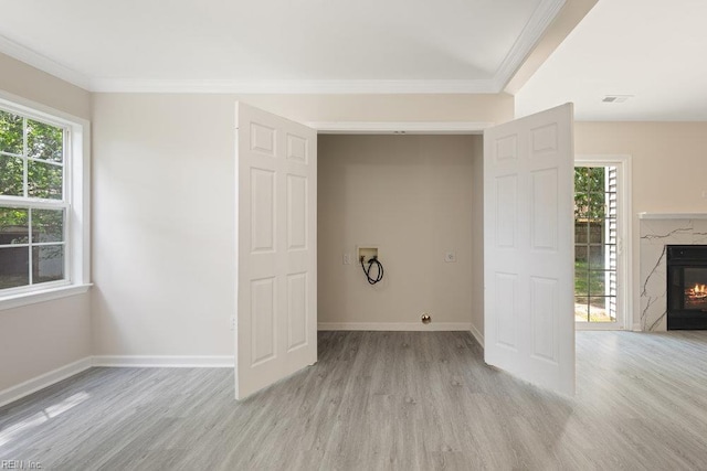 laundry area featuring washer hookup, light wood-type flooring, a high end fireplace, plenty of natural light, and ornamental molding