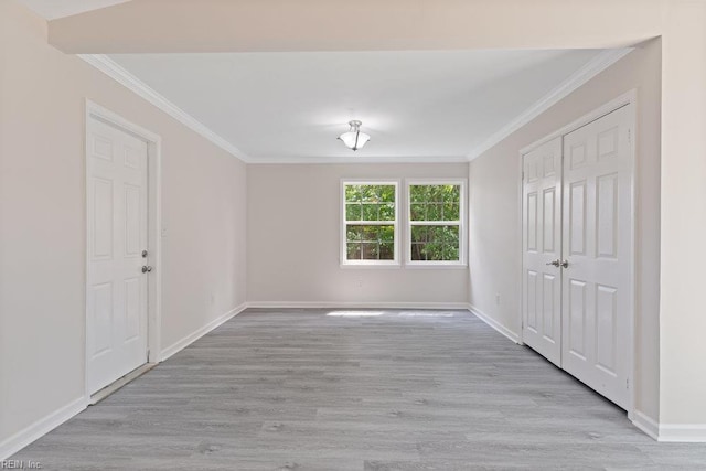 empty room with crown molding, light wood finished floors, and baseboards