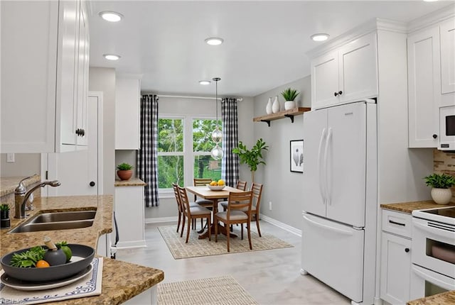 kitchen with white appliances, a sink, white cabinetry, baseboards, and light stone countertops