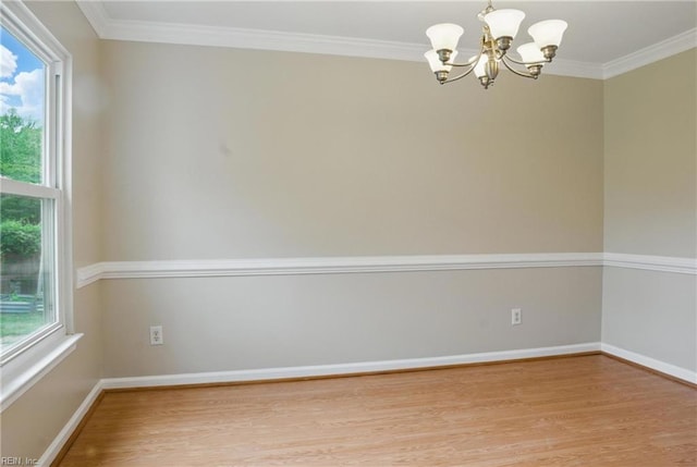 spare room with a chandelier, wood finished floors, ornamental molding, and baseboards
