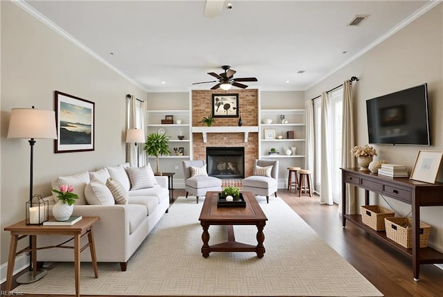 living room with a ceiling fan, wood finished floors, a brick fireplace, built in features, and ornamental molding