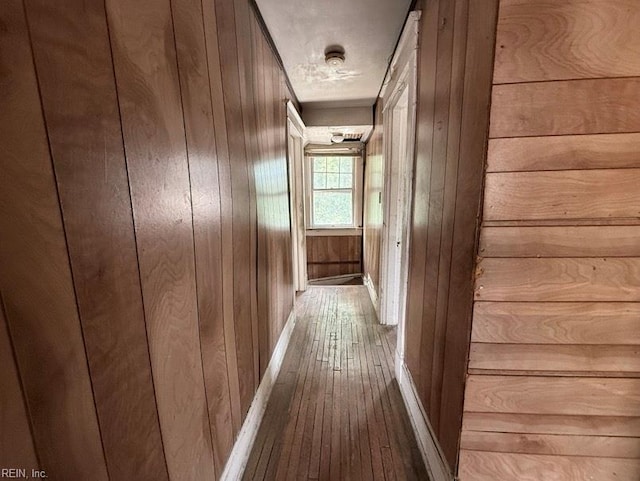 hall featuring wood-type flooring, wooden walls, and baseboards