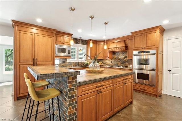 1276 Hebden Cv, Virginia Beach, VA 23452 - kitchen featuring appliances with stainless steel finishes, custom range hood, backsplash, dark tile patterned flooring, and brown cabinets