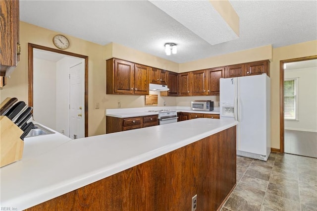 kitchen with white appliances, a peninsula, under cabinet range hood, light countertops, and baseboards