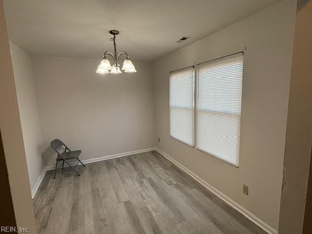 unfurnished room with wood finished floors, a chandelier, and baseboards