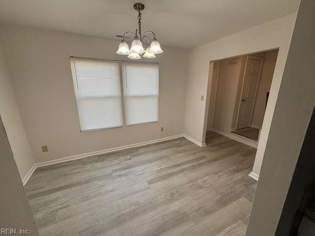 unfurnished dining area with a chandelier, wood finished floors, and baseboards