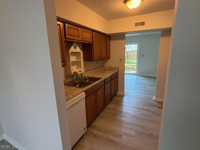 kitchen featuring dishwasher, a sink, light wood-type flooring, and baseboards