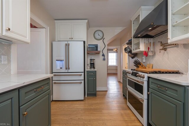 kitchen with high quality appliances, wall chimney exhaust hood, green cabinets, white cabinets, and backsplash