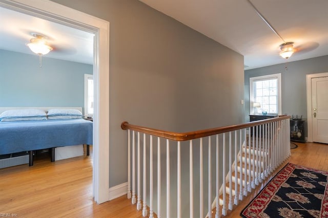 corridor with an upstairs landing, light wood-style flooring, and baseboards