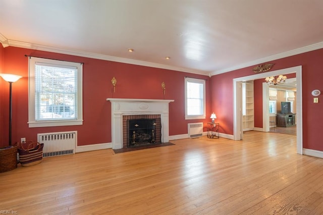 unfurnished living room with radiator, ornamental molding, wood-type flooring, a chandelier, and a fireplace