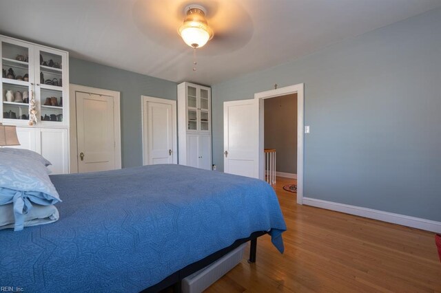 bedroom featuring baseboards, wood finished floors, multiple closets, and ceiling fan