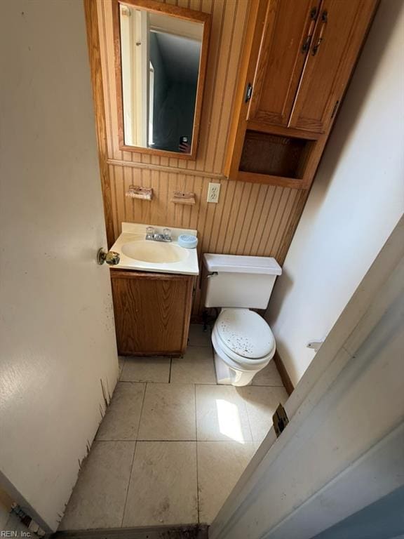 half bath with toilet, vanity, and wood walls