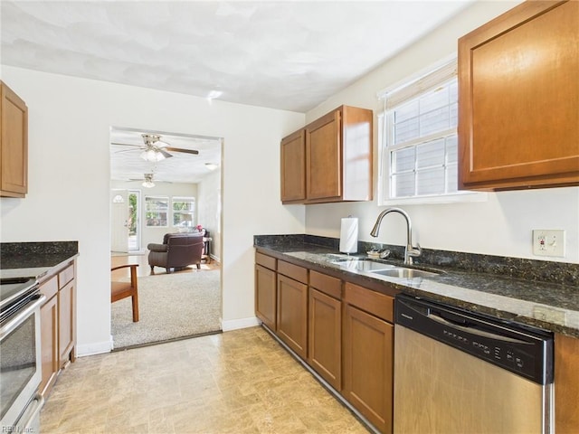 kitchen featuring appliances with stainless steel finishes, a sink, a ceiling fan, dark stone countertops, and brown cabinets