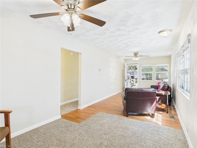 carpeted living area with ceiling fan and baseboards