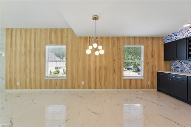 unfurnished dining area featuring marble tiled flooring, a chandelier, and healthy amount of natural light