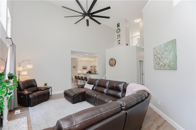 living room featuring a towering ceiling, a ceiling fan, wood finished floors, and baseboards