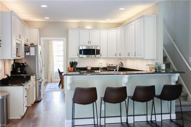 kitchen featuring stainless steel microwave, dark countertops, a breakfast bar, white cabinetry, and light wood-style floors