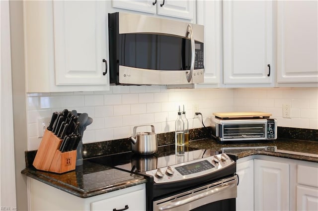 kitchen featuring stainless steel appliances, white cabinets, decorative backsplash, and dark stone counters