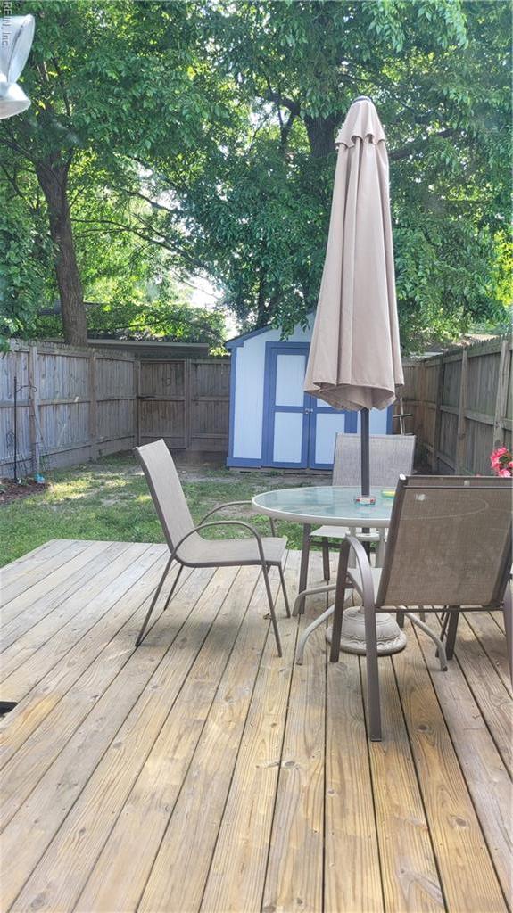 deck with a fenced backyard, a storage unit, outdoor dining area, and an outbuilding