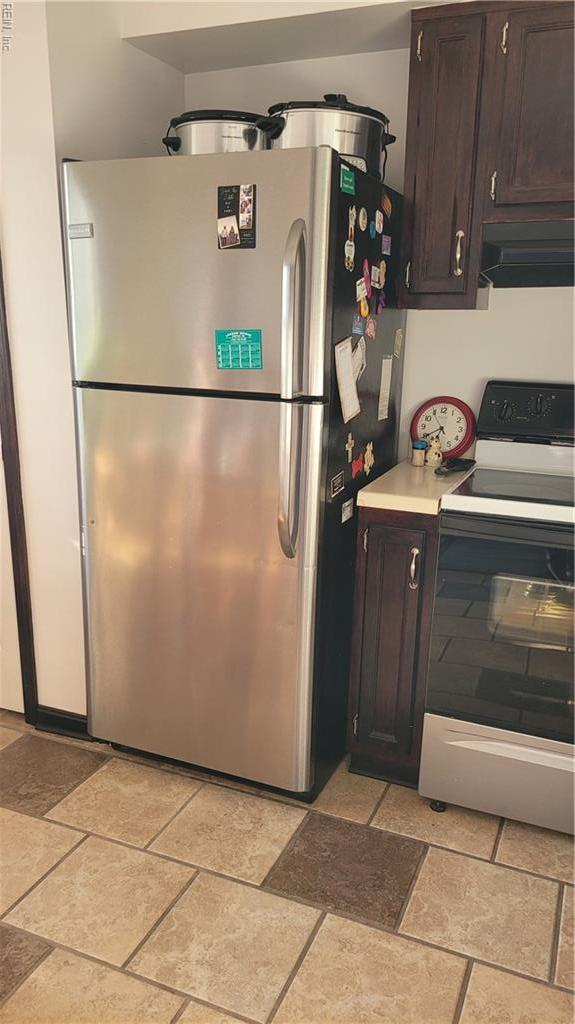 kitchen featuring electric stove, freestanding refrigerator, ventilation hood, and stone tile floors