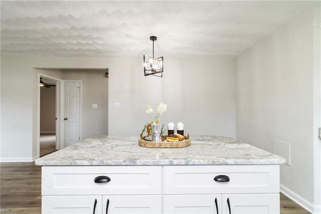 kitchen with baseboards, white cabinets, dark wood-style flooring, light stone countertops, and a chandelier