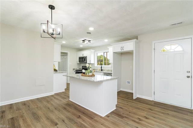 kitchen with appliances with stainless steel finishes, white cabinets, wood finished floors, a chandelier, and baseboards