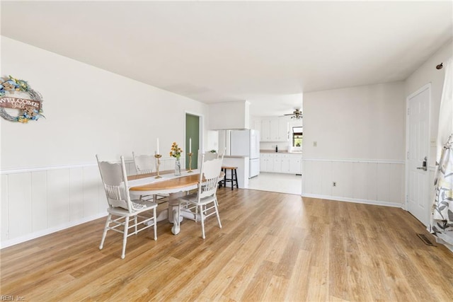 dining area with light wood-style flooring, a wainscoted wall, and a ceiling fan